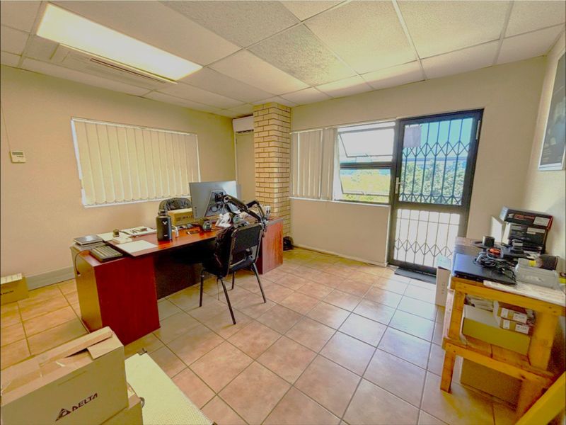 A functional office space featuring ceramic tiled flooring, a suspended ceiling, a brick feature pillar, and a secure entrance door with a security gate.