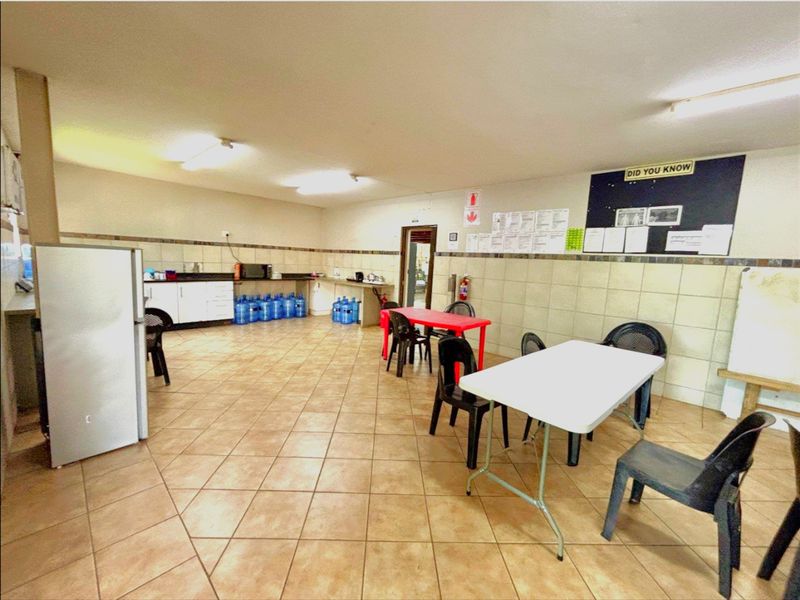 An open-plan industrial breakroom featuring tiled flooring, built-in kitchenette cabinetry, and functional lighting, suitable for staff use.