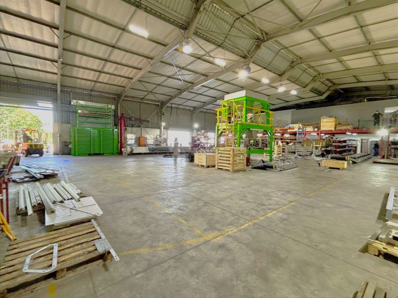 Spacious industrial warehouse featuring high ceilings, concrete flooring, steel frame construction, and large roller shutter access points suitable for manufacturing or storage operations.