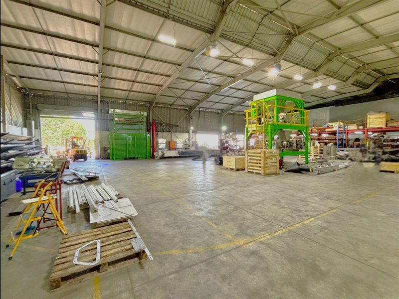 Spacious industrial warehouse featuring high-bay lighting, concrete flooring, and large roller shutter doors, suitable for manufacturing or storage operations.