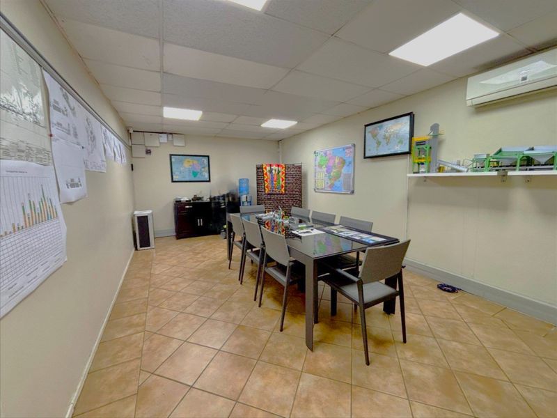 A functional office or meeting room featuring ceramic tile flooring, a suspended ceiling with recessed lighting, and a wall-mounted air conditioning unit.