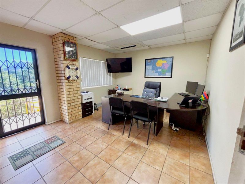 A functional office space featuring tiled flooring, a drop ceiling, and a decorative brick pillar, with a security gate at the entrance.