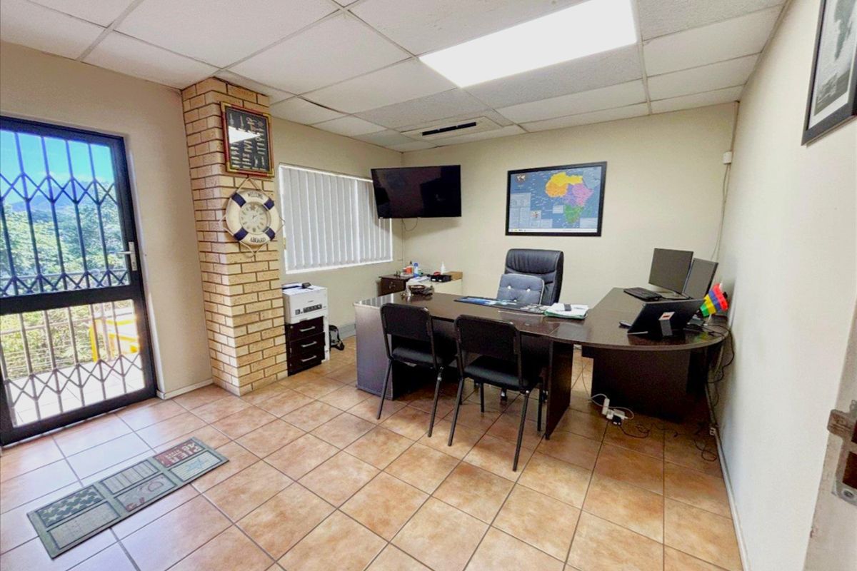 A functional office space featuring tiled flooring, a drop ceiling, and a decorative brick pillar, with a security gate at the entrance.