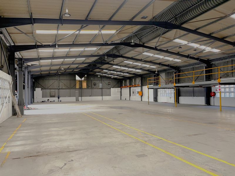 Spacious industrial warehouse featuring a high-clearance steel portal frame, concrete flooring, and an integrated mezzanine level suitable for storage or office conversion.