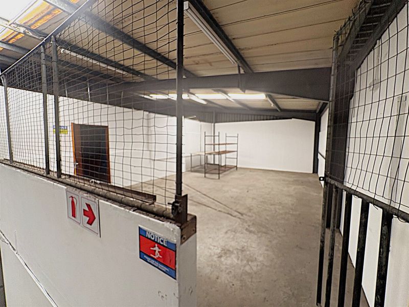 An industrial utility space featuring concrete flooring, steel mesh partitioning, and exposed structural beams, suitable for storage or workshop use.