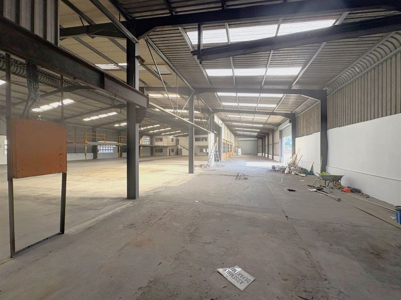 Expansive industrial warehouse space featuring a high-clearance steel portal frame, concrete flooring, integrated mezzanine level, and natural light provided by roof skylights.