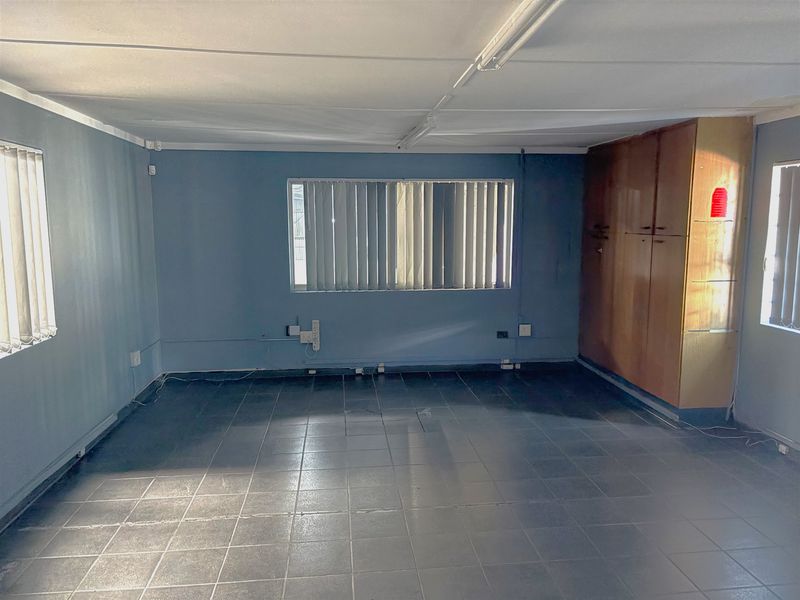 An empty office space featuring tiled flooring, built-in storage cabinetry, and vertical window blinds, suitable for a professional workspace.