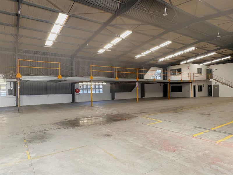 Spacious industrial warehouse featuring a mezzanine level with safety railings, high ceilings with exposed steel structure, and durable concrete flooring.