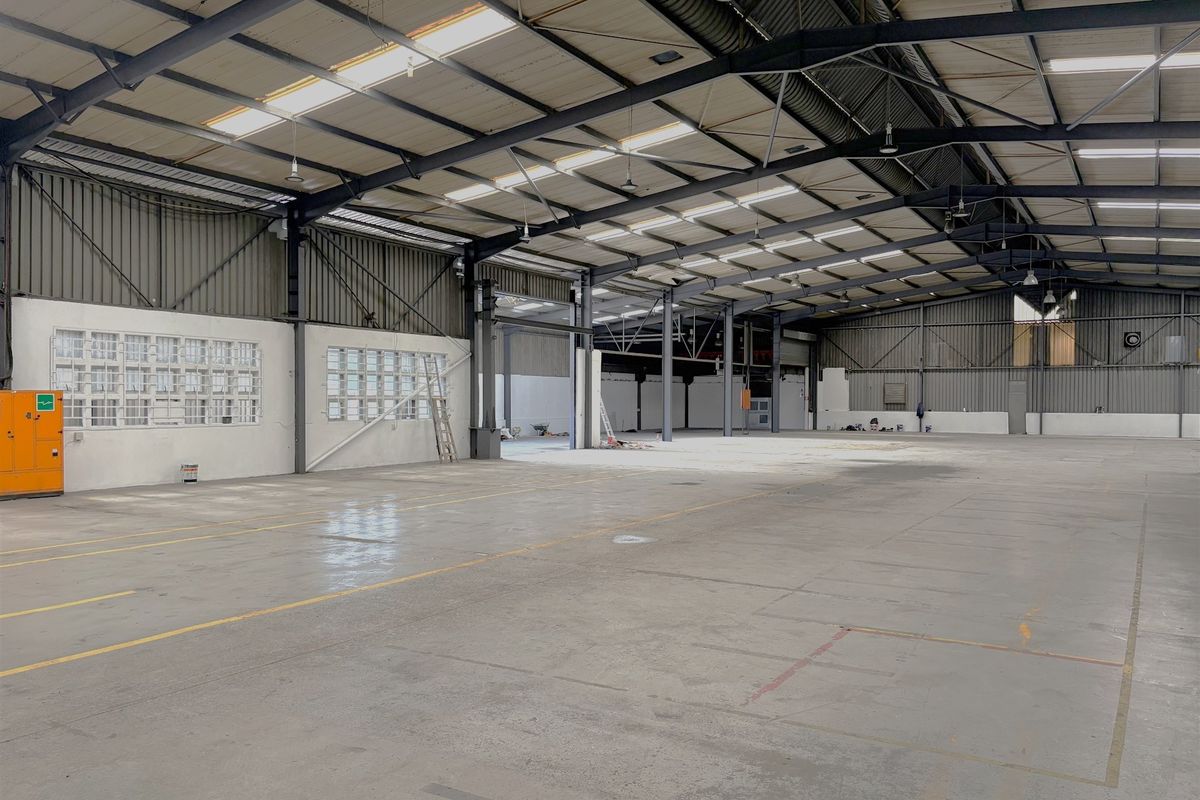 A spacious industrial warehouse featuring high ceilings with exposed steel trusses, concrete flooring, and natural light provided by integrated skylights.
