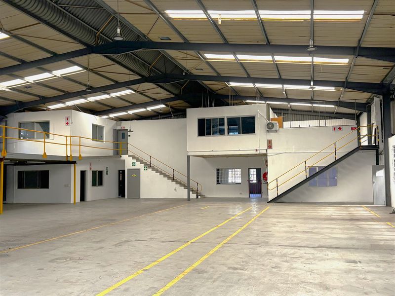 Spacious industrial warehouse featuring a large open floor area, mezzanine levels with steel staircases, high-clearance roof with skylights, and functional office or utility spaces.