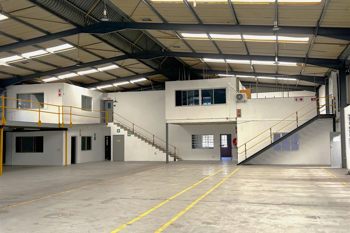Spacious industrial warehouse featuring a large open floor area, mezzanine levels with steel staircases, high-clearance roof with skylights, and functional office or utility spaces.