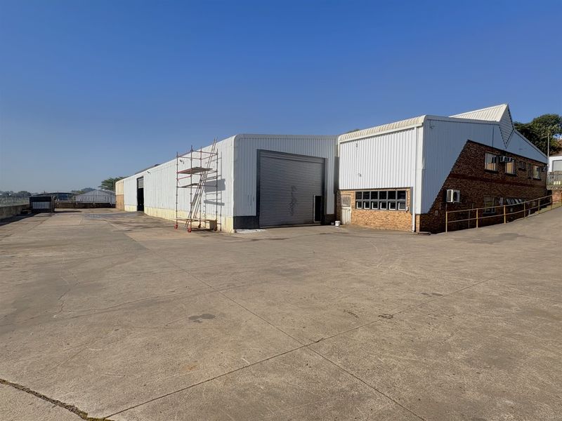 Industrial warehouse exterior featuring a large concrete yard, roller shutter access, and a combination of metal cladding and brick facade construction.