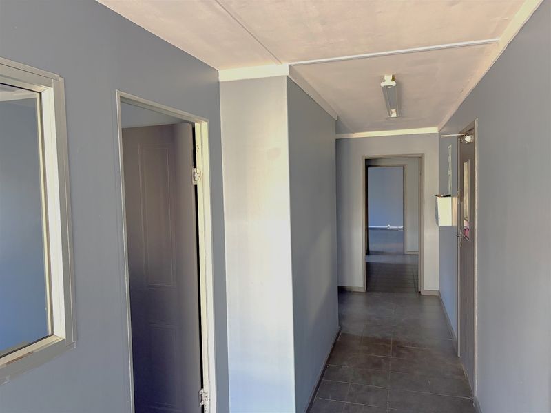 A clean, well-lit industrial hallway featuring tiled flooring, neutral grey walls, and multiple internal access points.