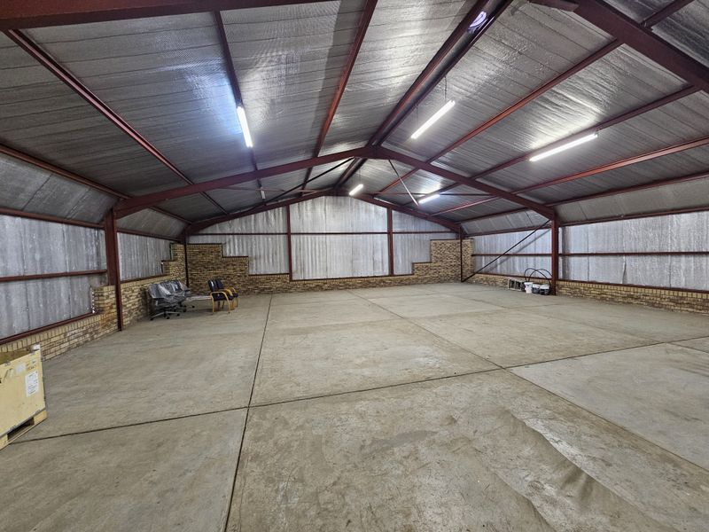 Spacious industrial warehouse featuring exposed steel trusses, insulated metal wall cladding, brick base walls, and polished concrete flooring with overhead fluorescent lighting.