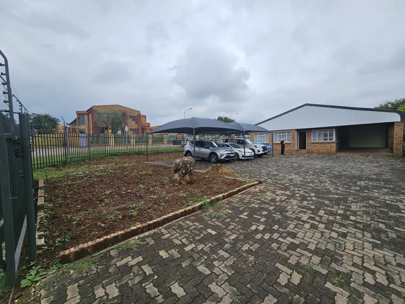 Exterior view of an industrial property featuring a paved driveway, covered parking area, and perimeter security fencing.