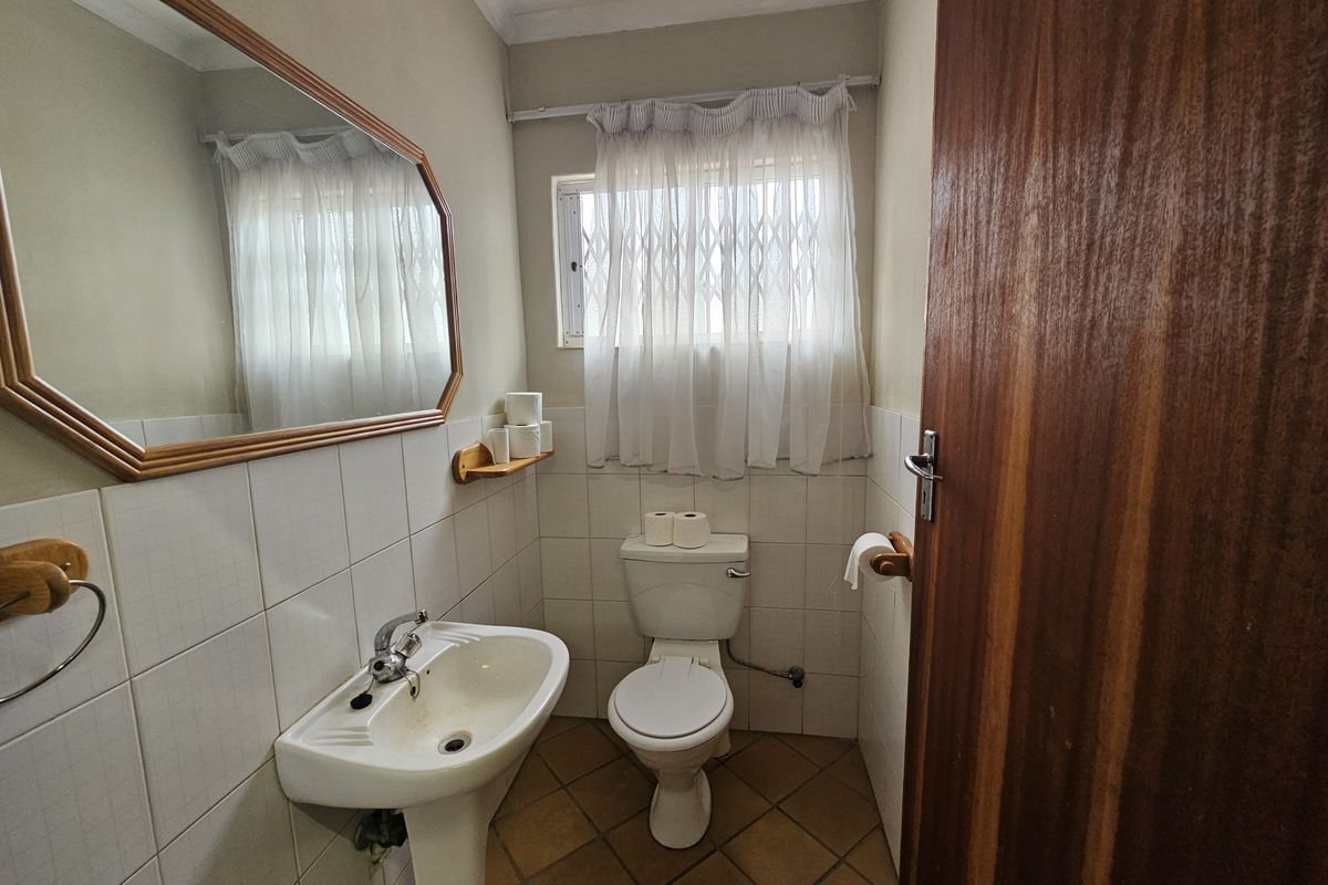 A functional guest bathroom featuring a pedestal washbasin, a standard toilet, and wall-mounted mirror with tiled finishes.