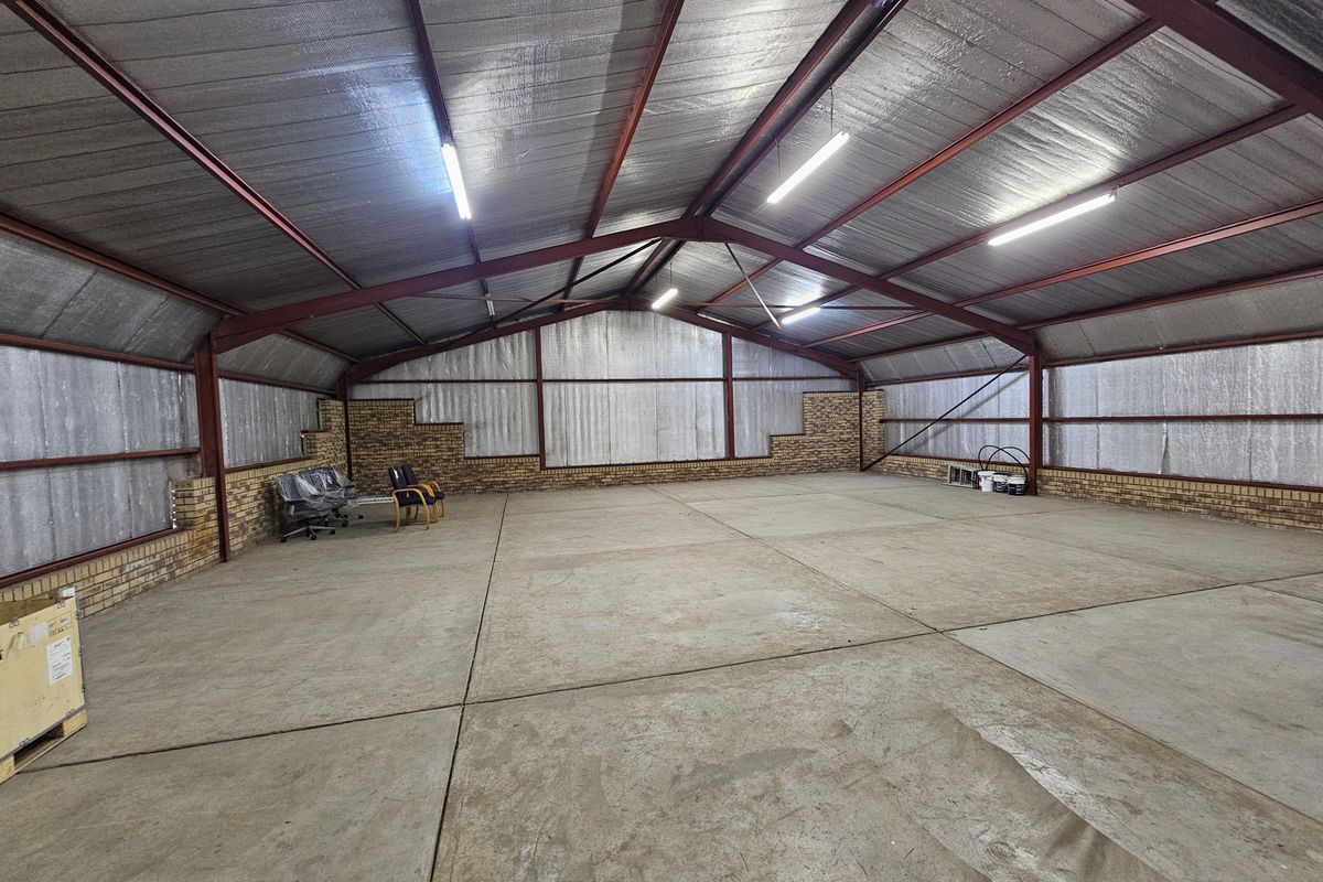 Spacious industrial warehouse featuring exposed steel trusses, insulated metal wall cladding, brick base walls, and polished concrete flooring with overhead fluorescent lighting.