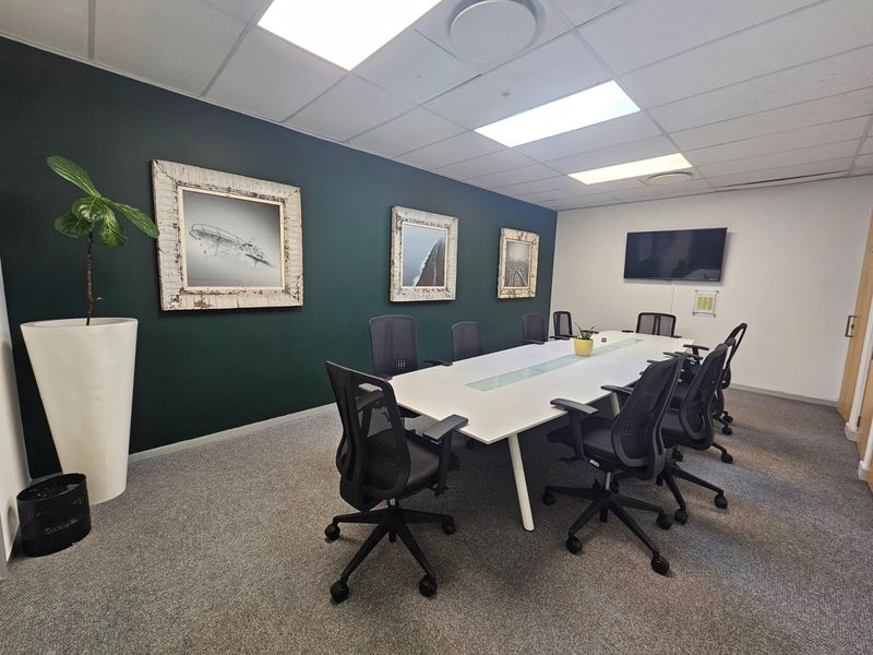 A professional boardroom featuring a dark accent wall, suspended ceiling with recessed lighting, and a wall-mounted television for presentations.
