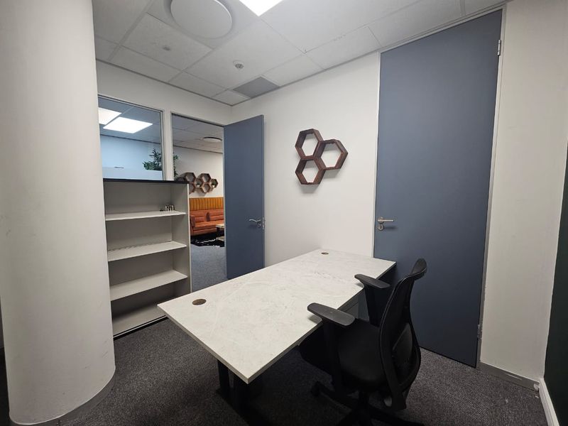 A functional office space featuring a suspended ceiling, built-in shelving, and an internal glass partition providing a view into the adjacent workspace.