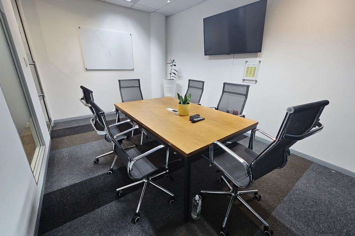 A professional meeting room featuring a modern boardroom table, suspended ceiling with recessed lighting, and durable carpet tiles.