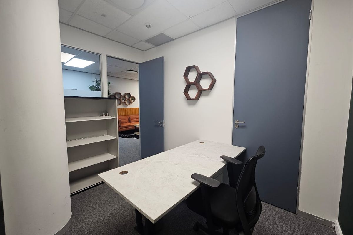 A functional office space featuring a suspended ceiling, built-in shelving, and an internal glass partition providing a view into the adjacent workspace.