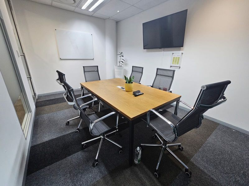 A professional meeting room featuring a modern boardroom table, suspended ceiling with recessed lighting, and durable carpet tiles.