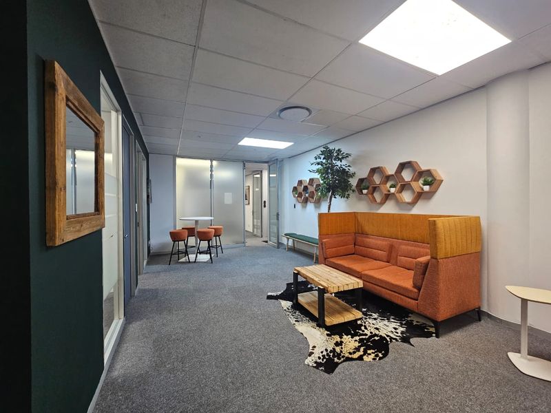 Modern office breakout area featuring glass partition walls, carpeted flooring, and recessed lighting in a professional business environment.