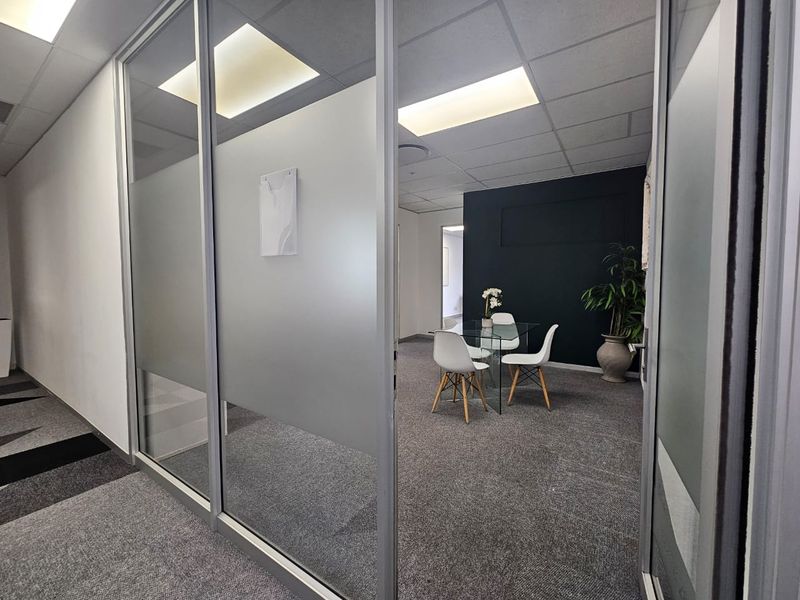 Modern office space featuring glass partition walls, suspended ceilings with recessed lighting, and professional carpet flooring.