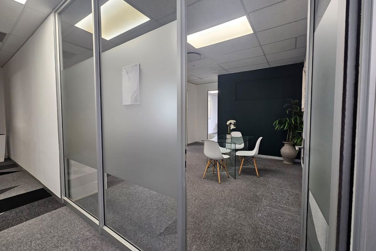 Modern office space featuring glass partition walls, suspended ceilings with recessed lighting, and professional carpet flooring.