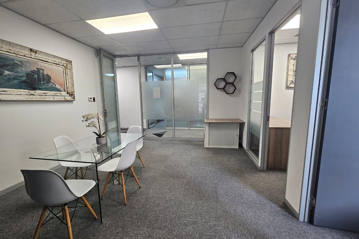 Professional office space featuring glass partition walls, suspended ceilings, and carpeted flooring, providing a clean and functional work environment.