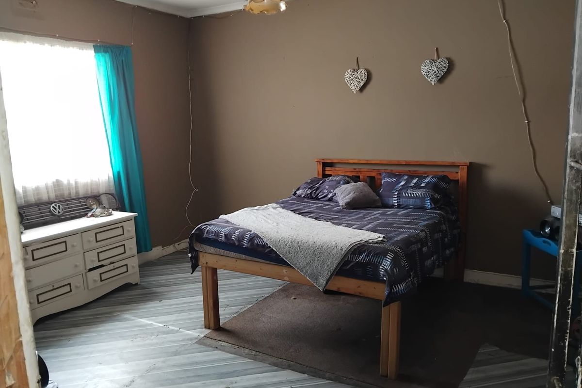 A bedroom featuring wood-look flooring and a window, currently requiring cosmetic updates to the wall finishes and electrical fixtures.