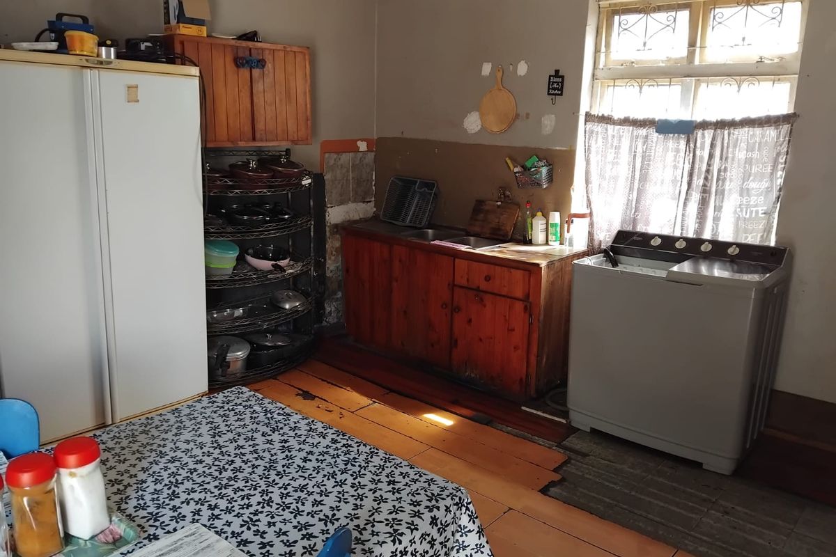 A dated kitchen area featuring wooden cabinetry, a double sink, and timber flooring, requiring cosmetic updates to improve its overall condition and functionality.