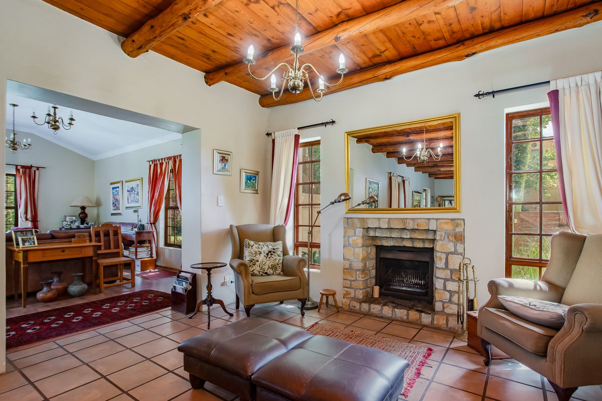Cozy living room featuring a rustic exposed timber beam ceiling, a stone-clad fireplace, and classic ceramic floor tiles with views to an adjacent study area.