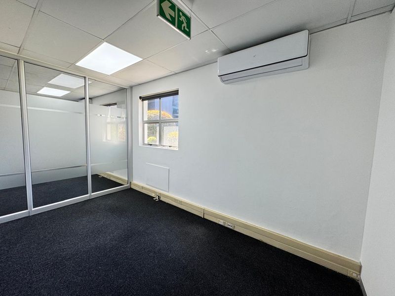 A clean, empty office space featuring a glass partition, suspended ceiling with recessed lighting, split-system air conditioning, and carpeted flooring.