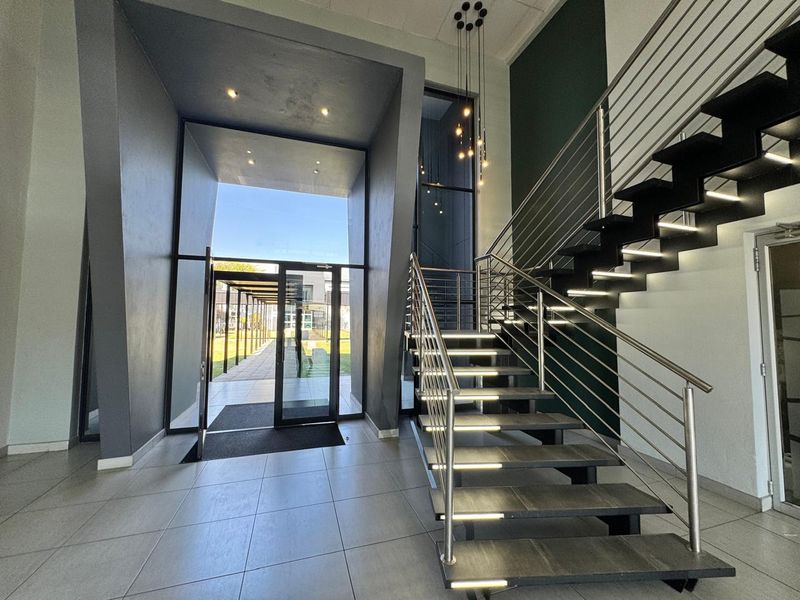 Modern office entrance foyer featuring a striking architectural staircase with integrated lighting, glass entry doors, and high-quality tiled flooring.
