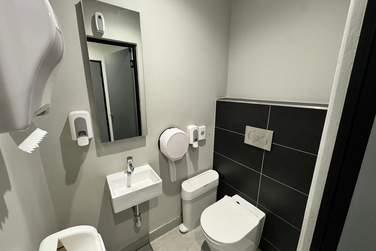 A modern, compact office restroom featuring a wall-hung toilet with a concealed cistern, a wall-mounted basin, and a sleek tiled feature wall.
