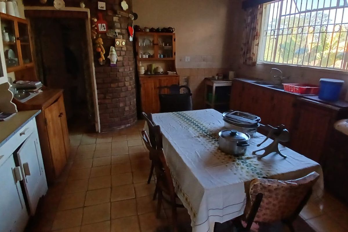 A rustic farm-style kitchen featuring exposed brickwork, traditional wooden cabinetry, tiled flooring, and a functional double basin sink with security-barred windows.