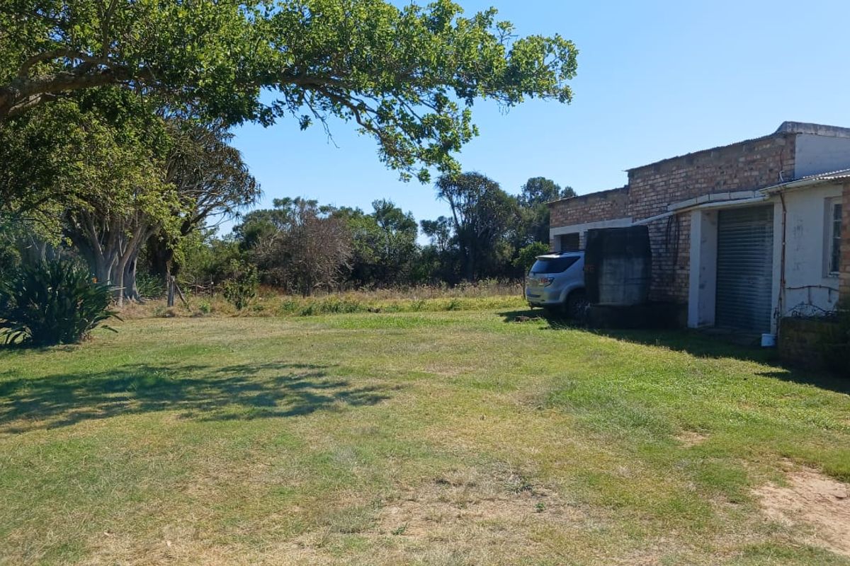 Rear view of the farm building featuring exposed brickwork, a roller shutter door, and an adjacent concrete water tank set within a large grassy yard.