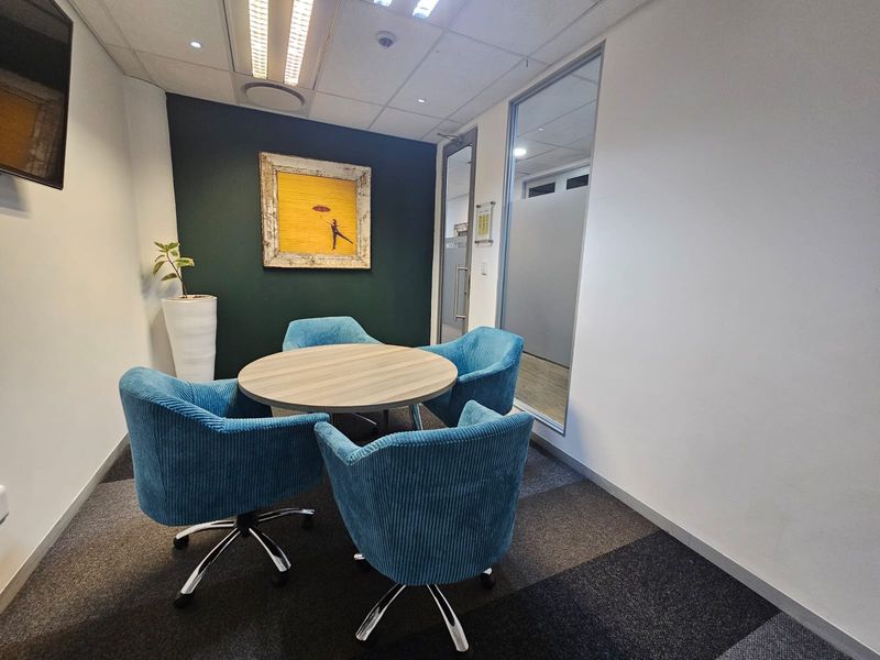 A modern, well-lit office meeting room featuring carpeted flooring, a glass partition wall, and a professional suspended ceiling with recessed lighting.