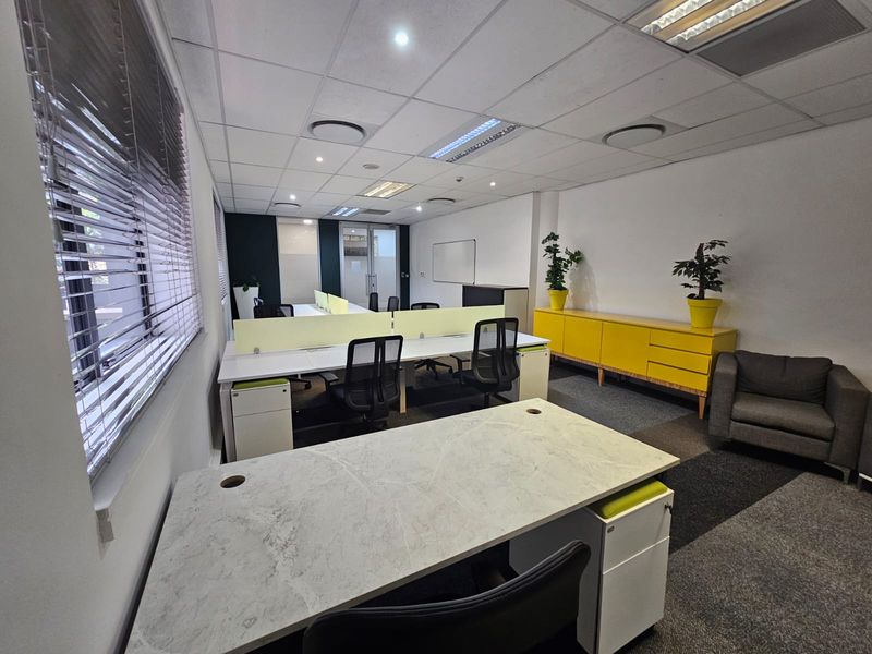 A functional office space featuring a suspended ceiling with recessed lighting, carpeted flooring, and large windows with venetian blinds.