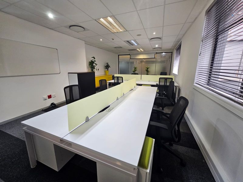 A modern, well-lit office space featuring a suspended ceiling, carpeted flooring, and a glass partition, providing a professional and functional work environment.