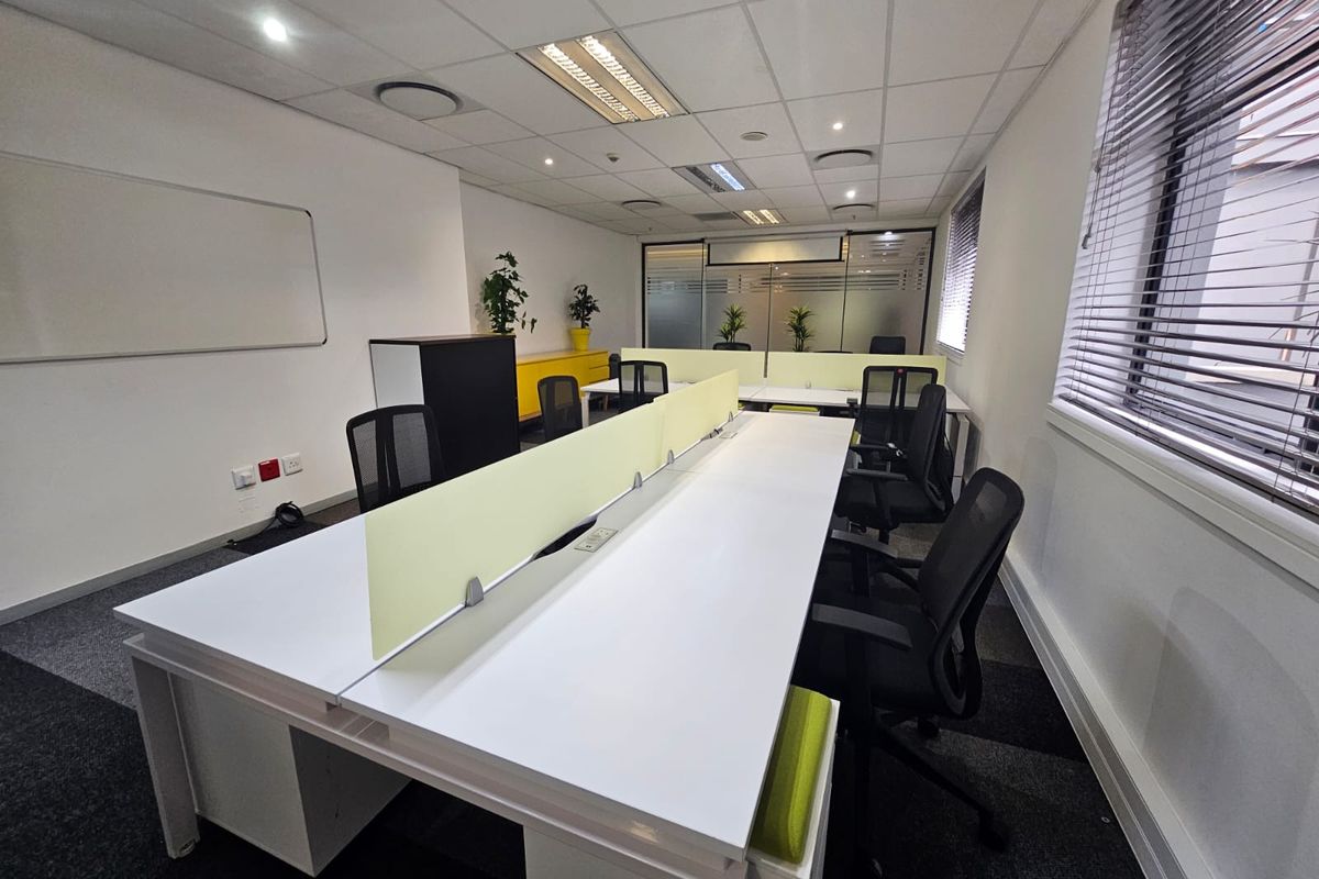 A modern, well-lit office space featuring a suspended ceiling, carpeted flooring, and a glass partition, providing a professional and functional work environment.