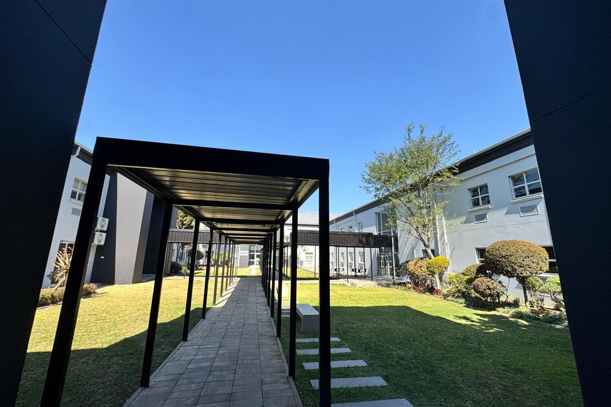A well-maintained office courtyard featuring a covered walkway, paved pathways, and landscaped garden areas between the building wings.