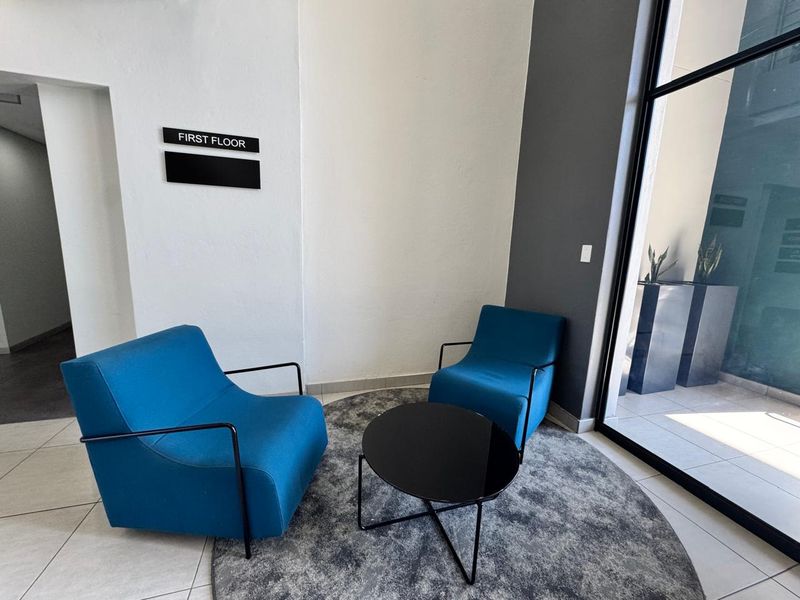A modern office building entry area featuring tiled flooring, large glass windows, and clear directional signage for the first floor.