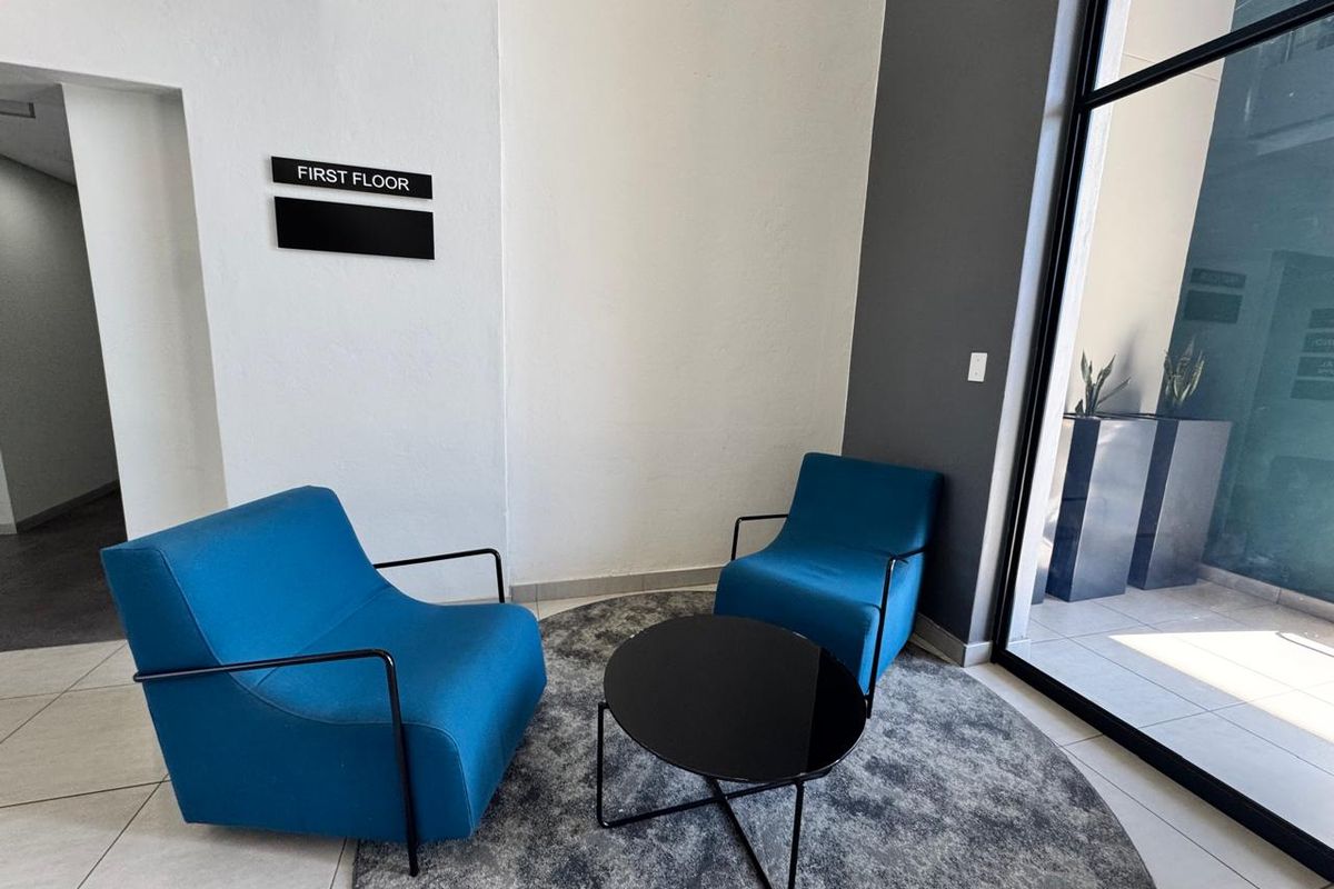A modern office building entry area featuring tiled flooring, large glass windows, and clear directional signage for the first floor.