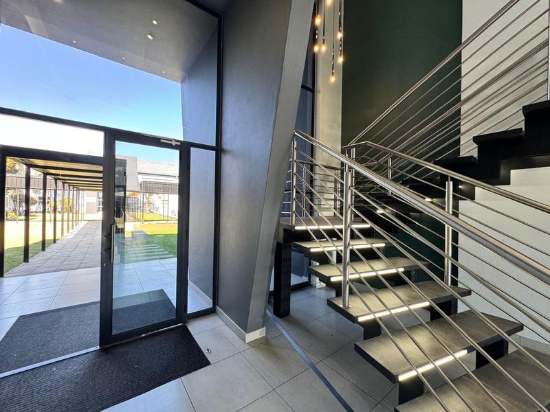 Modern office entrance featuring a striking staircase with stainless steel railings, integrated stair lighting, and large glass panels opening to an outdoor walkway.