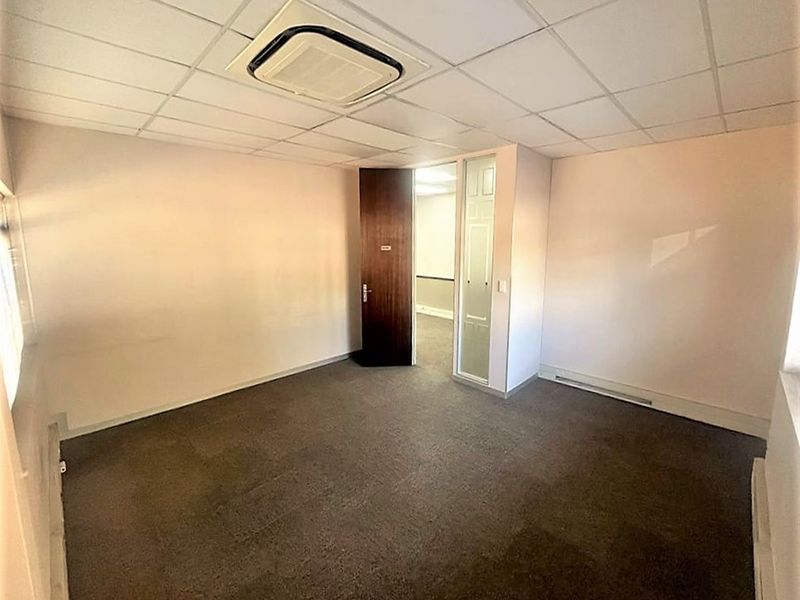 An empty office space featuring a suspended ceiling with integrated air conditioning, carpeted flooring, and a combination of timber and glass panel doors.