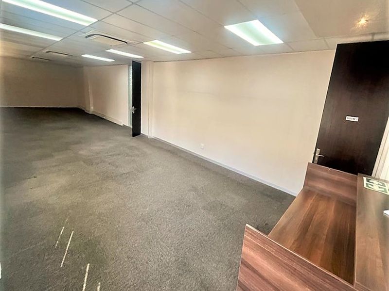 An empty office space featuring a built-in reception desk, suspended ceiling with recessed lighting, and carpeted flooring.