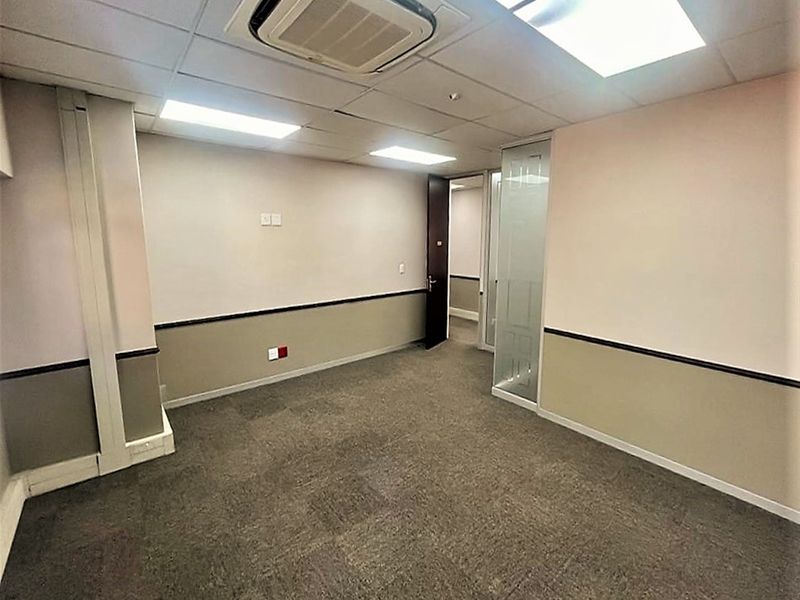 A vacant office space featuring carpeted flooring, a suspended ceiling with recessed lighting, integrated air conditioning, and a glass partition door.