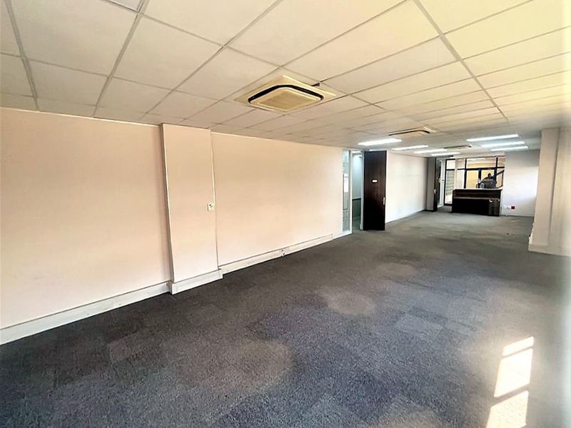 An empty, open-plan office space featuring a suspended ceiling, recessed lighting, and carpeted flooring, suitable for a professional workspace layout.